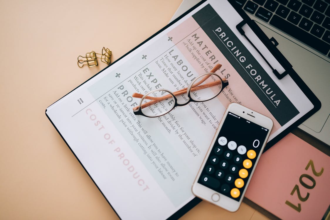 A clipboard with paper containing pricing calculation, glasses, and calculator on a table for types of pricing