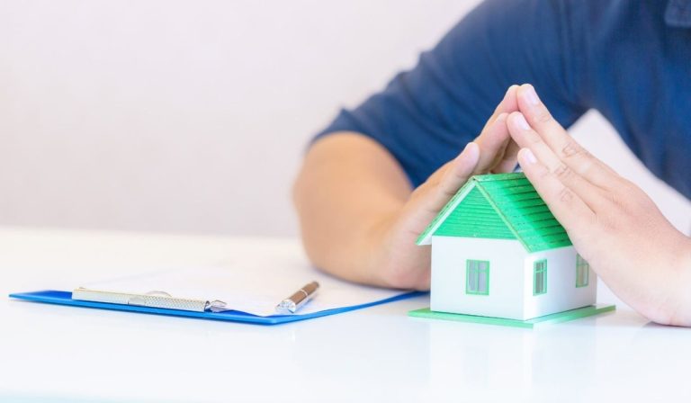 Hands of a person covering a house model symbolizing mortgage insurance.