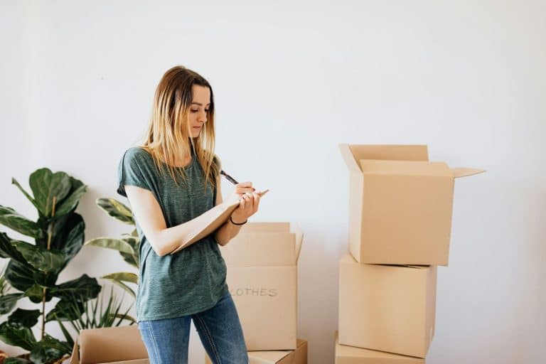 New homeowner making a moving checklist while unpacking cardboard boxes in her living room.