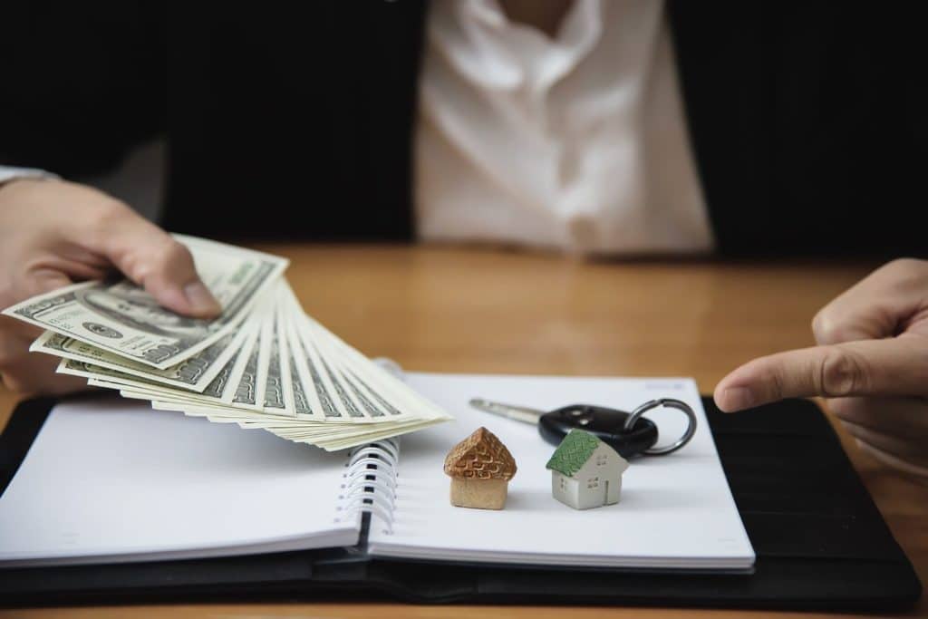 A professional holding cash next to house and car models, illustrating how personal loans fund major life goals.