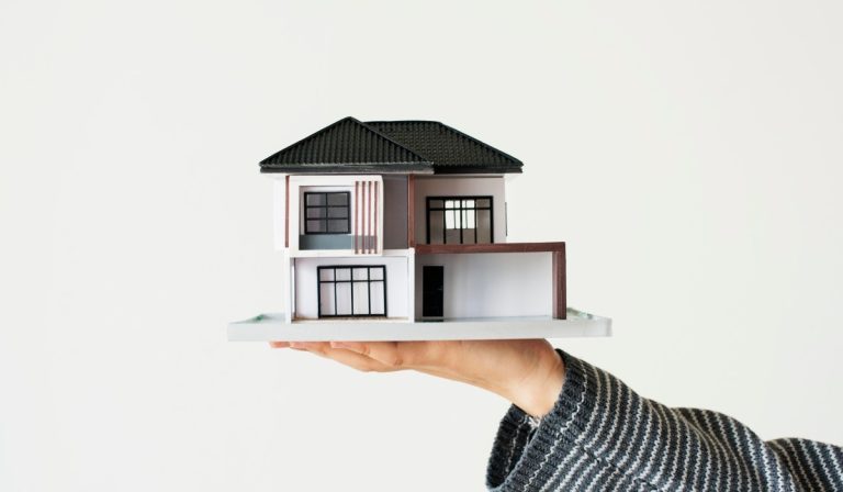 A person holding a small model house, representing the first steps to afford your dream home and build equity.