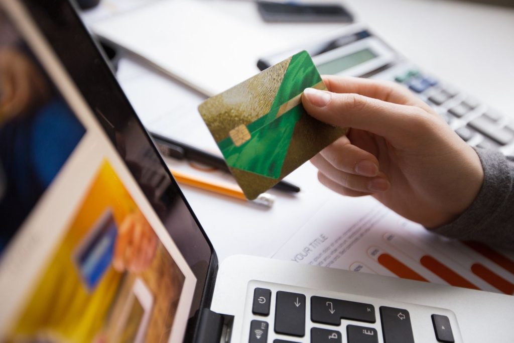 A close-up of a person holding a credit card over a laptop and financial documents, representing a review of spending to maintain a healthy credit utilization.