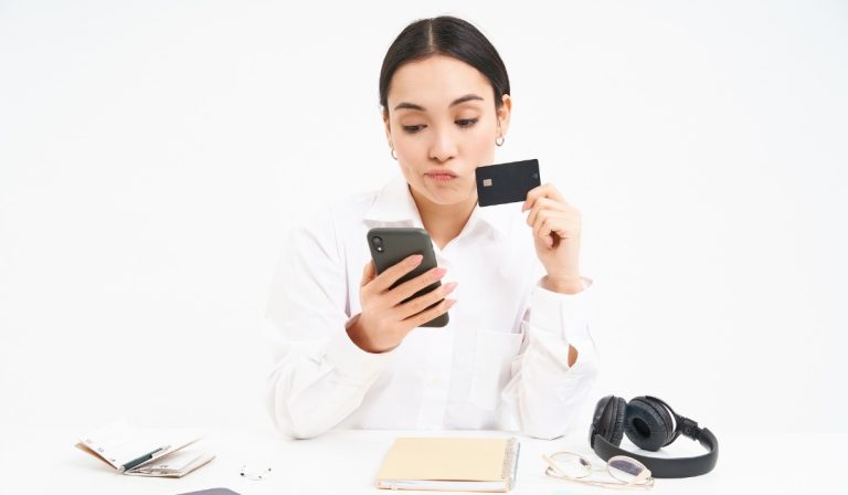 A woman looks confused at her phone and card, comparing a personal loan vs credit card for her next big expense.