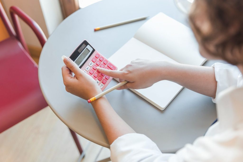 : A student uses a pink calculator and notebook to budget, a key habit for managing total debt and keeping credit utilization low.