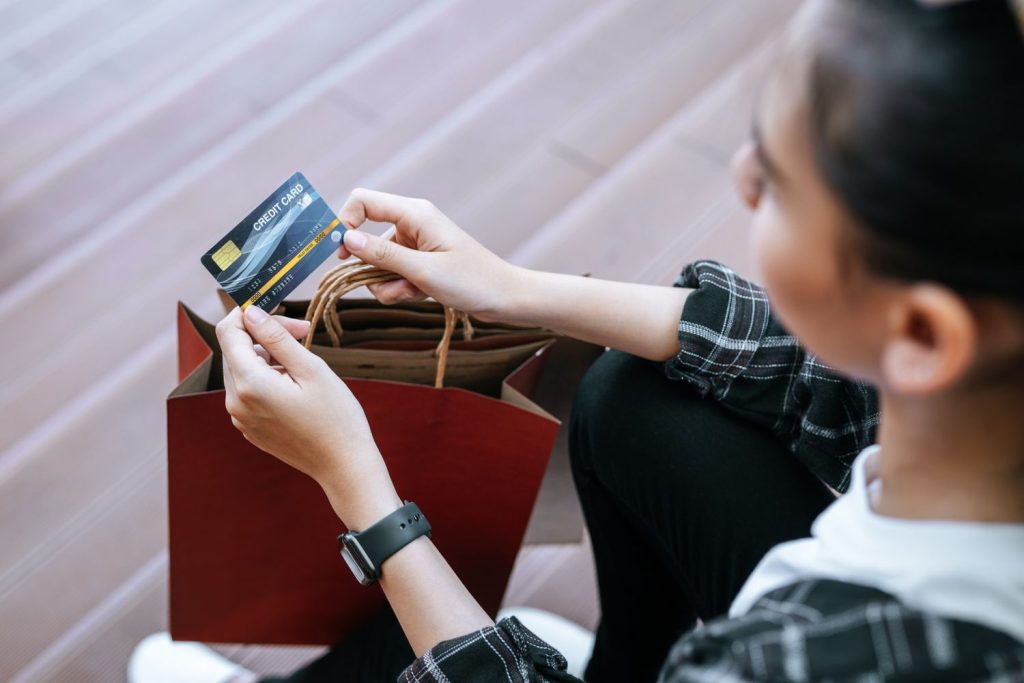 A shopper holds a card near bags, weighing the pros of a personal loan vs credit card for retail purchases.