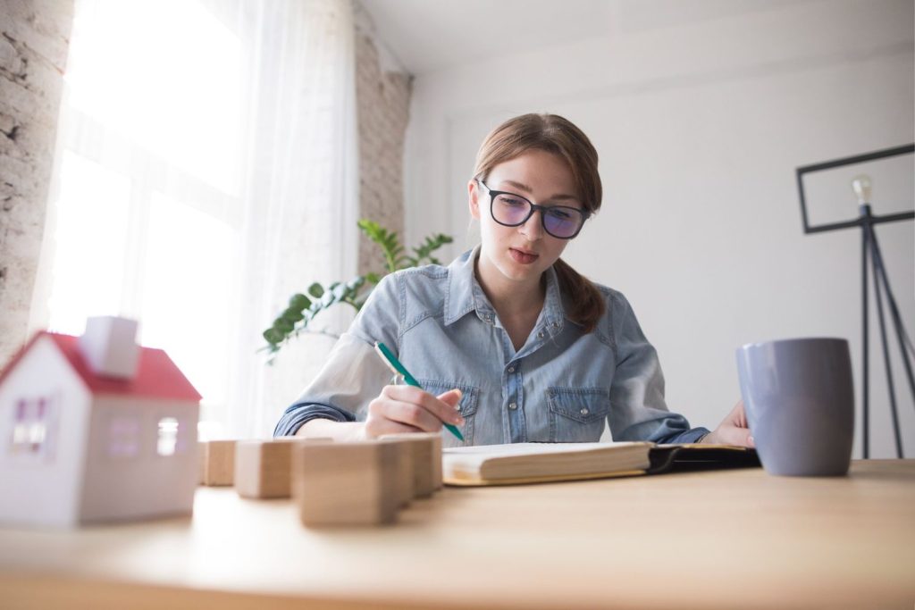 Woman planning budget for first time home buyer loans while sitting at a desk with a small house model.