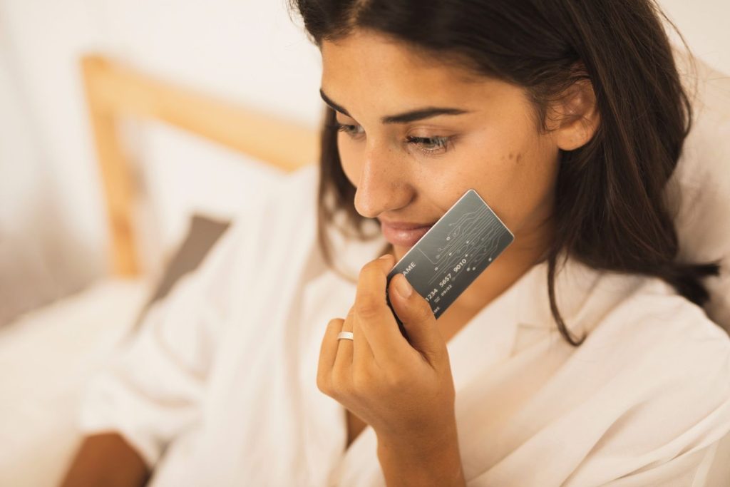 Close-up of a woman thoughtfully holding a card to her face, reflecting on staying motivated to pay credit card debt.