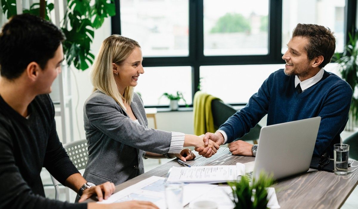 Real estate investors celebrate a successful closing with their private money lending partner at a wooden desk.