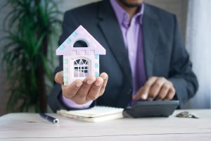 Man in suit holding a miniature house analyzing market value of a property