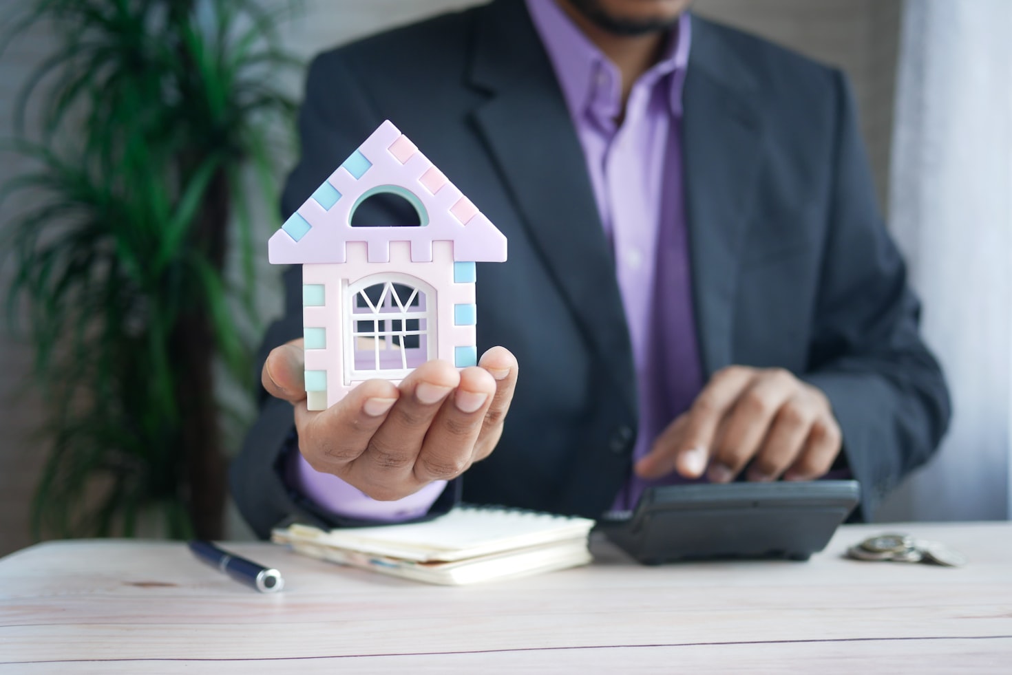 Man in suit holding a miniature house analyzing market value of a property