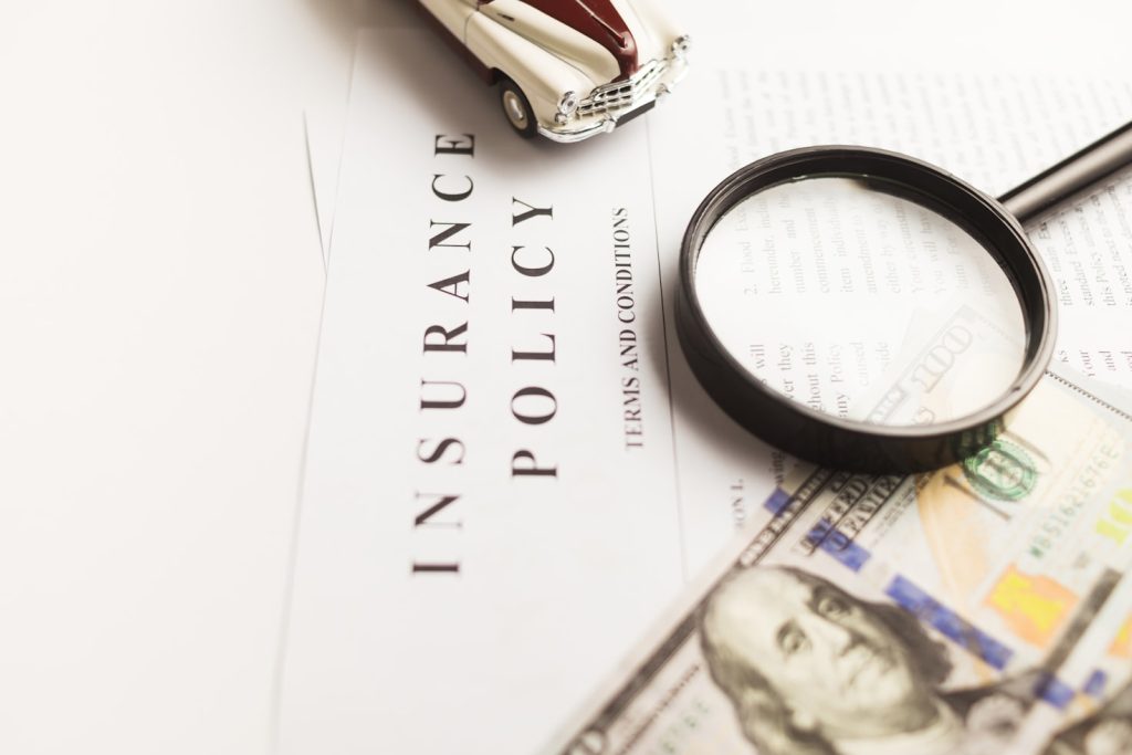 A picture of insurance policy document with magnifying glass, cash, and miniature care