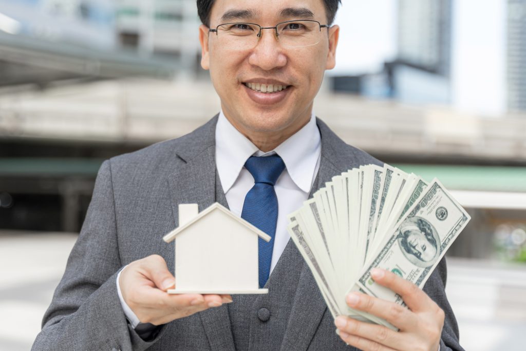 Man holding paper bills and miniature house representing rental income under the Augusta Rule