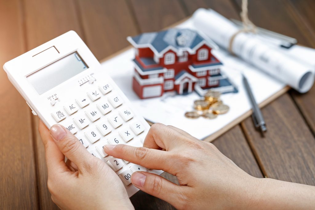 A female hand operating a calculator in front of a Villa house model representing rental income under the Augusta Rule