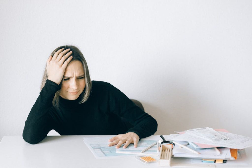 Woman in black long sleeve shirt sitting with hand on her head thinking about phantom debt