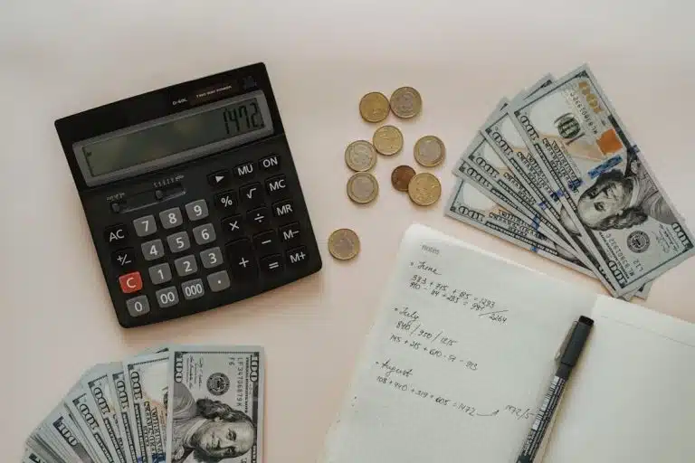 Calculator, money, notebook, and pen on top of a table for gross income vs. net income calculation