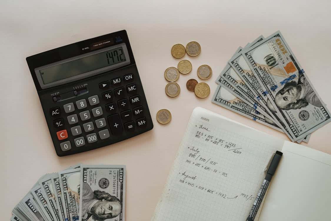 Calculator, money, notebook, and pen on top of a table for gross income vs. net income calculation