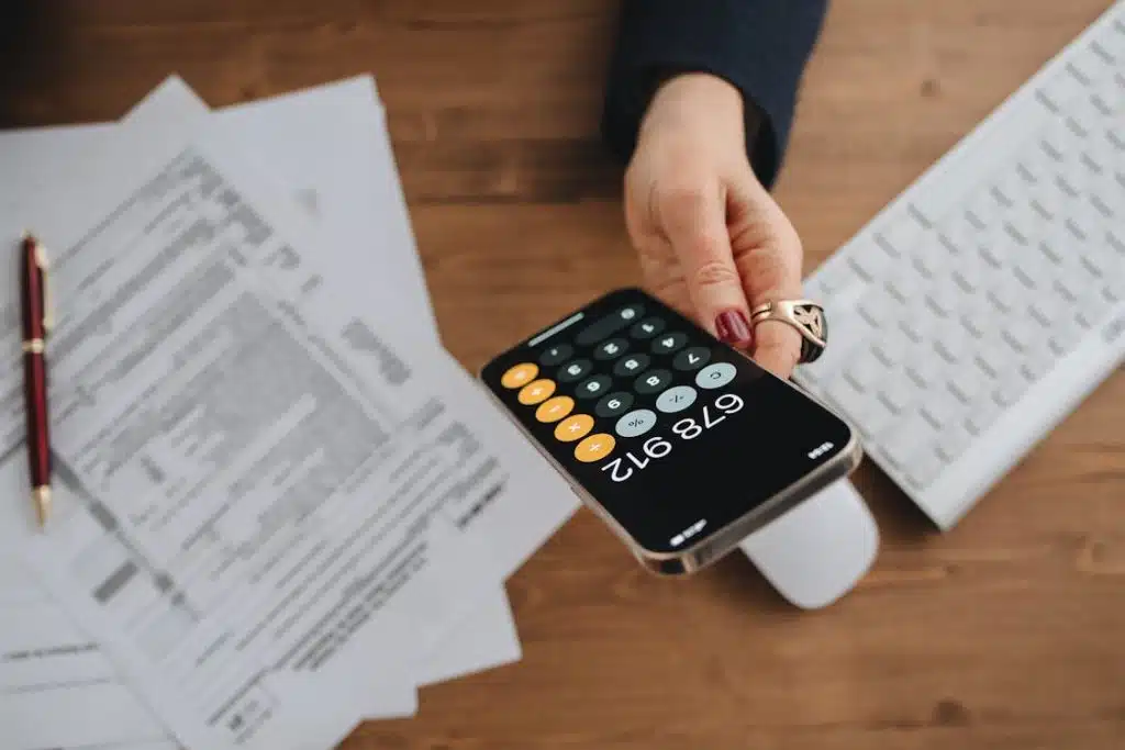 A person's hand holding a calculator calculating for gross income vs. net income