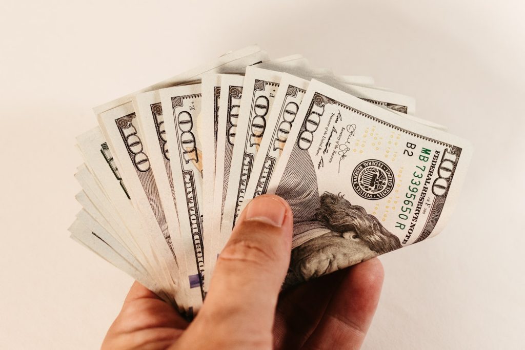 Hand holding bundle of twenty-dollar bills fluctuating income