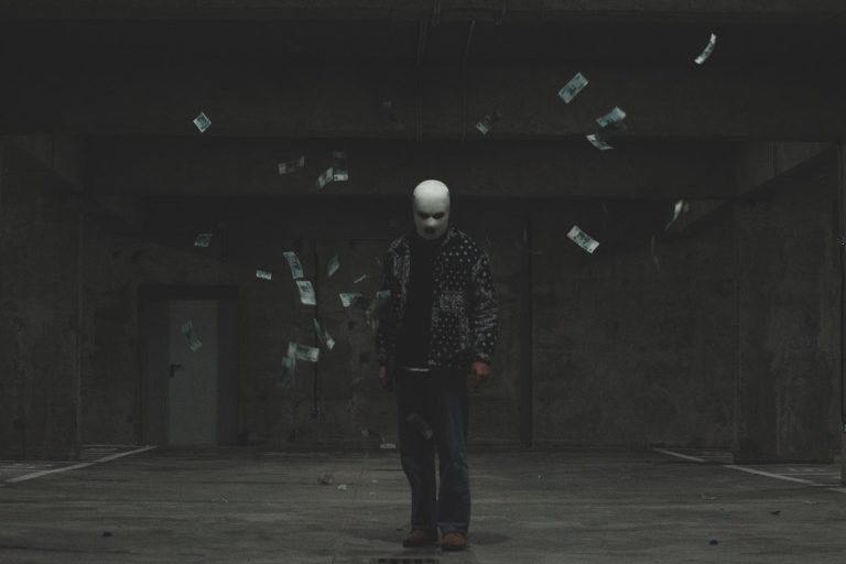 A man in a mask standing in a dark room with paper bills flying in the air symbolizing phantom debt