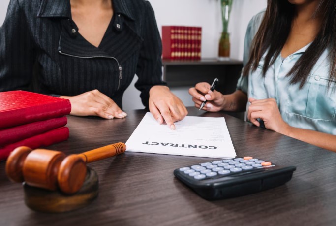 Woman pointing structured settlement document with pen, gavel and calculator on a brown table