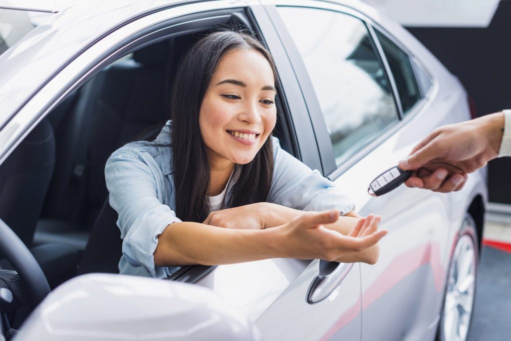 Happy woman accepting her car keys inside her c=brand new car with guaranteed asset protection
