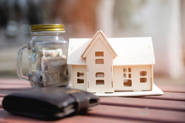 Portrait of mini house model beside a jar with coins and wallet