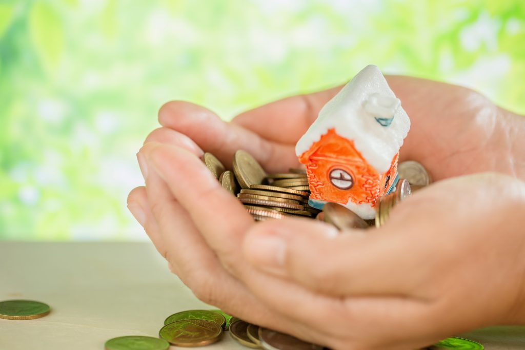 Hand holding house model on top of coins