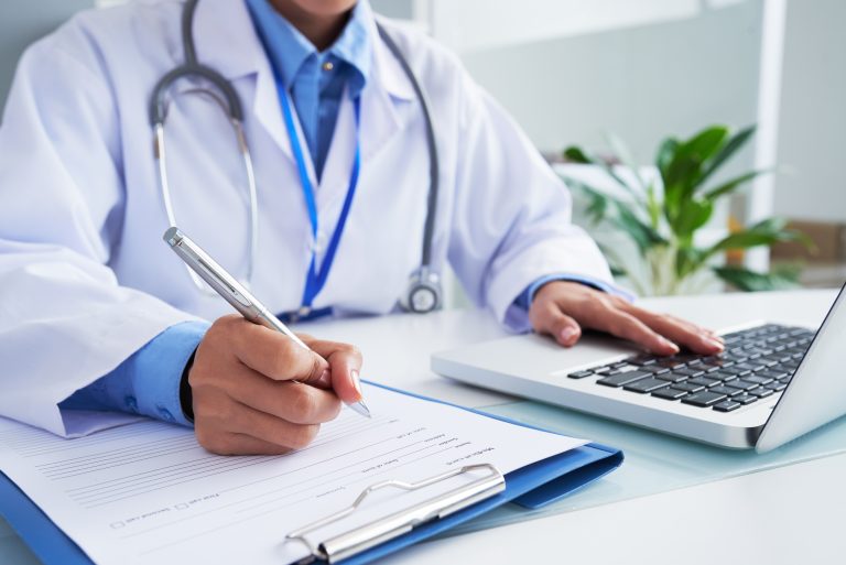 Doctor checking out-of-pocket maximum information in computer program before filling medical card