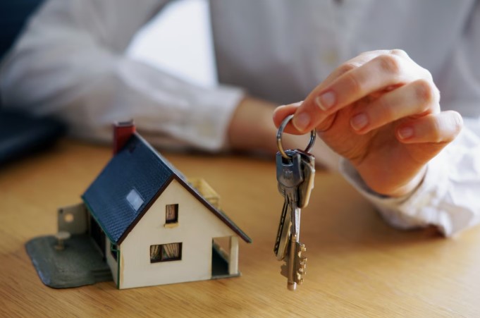 Man holding house keys with house model on his table