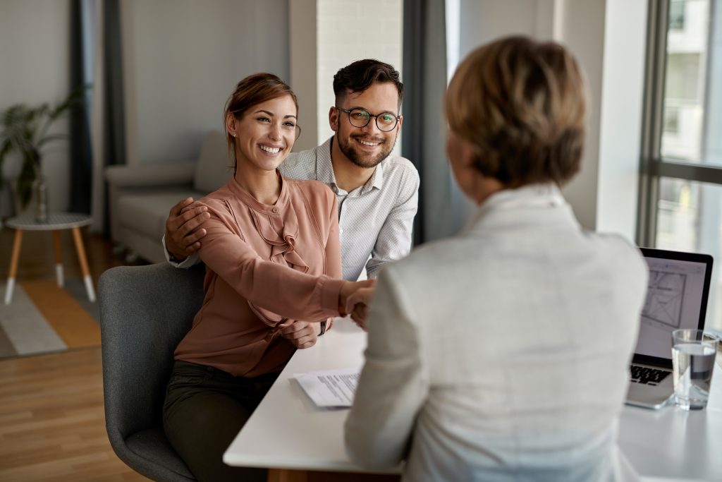 Young happy couple shaking hands with mortgage lender during a meeting in the office