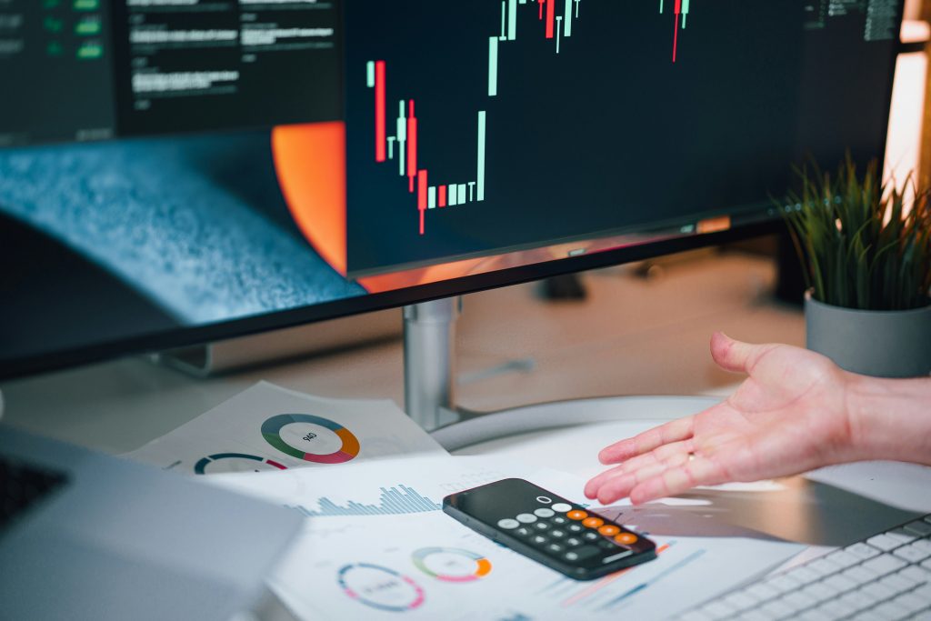 Calculator on top papers beside a monitor with graph