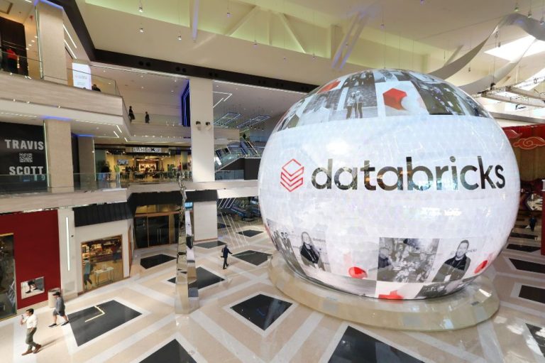 Large illuminated Databricks globe display inside a modern shopping mall atrium, featuring the company logo and photos.
