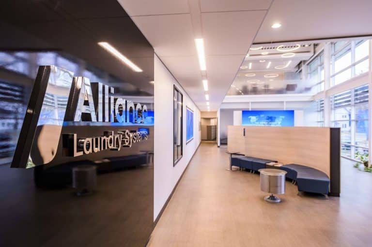 Modern office lobby of Alliance Laundry Systems with company logo on glass wall, seating area, and bright natural lighting.