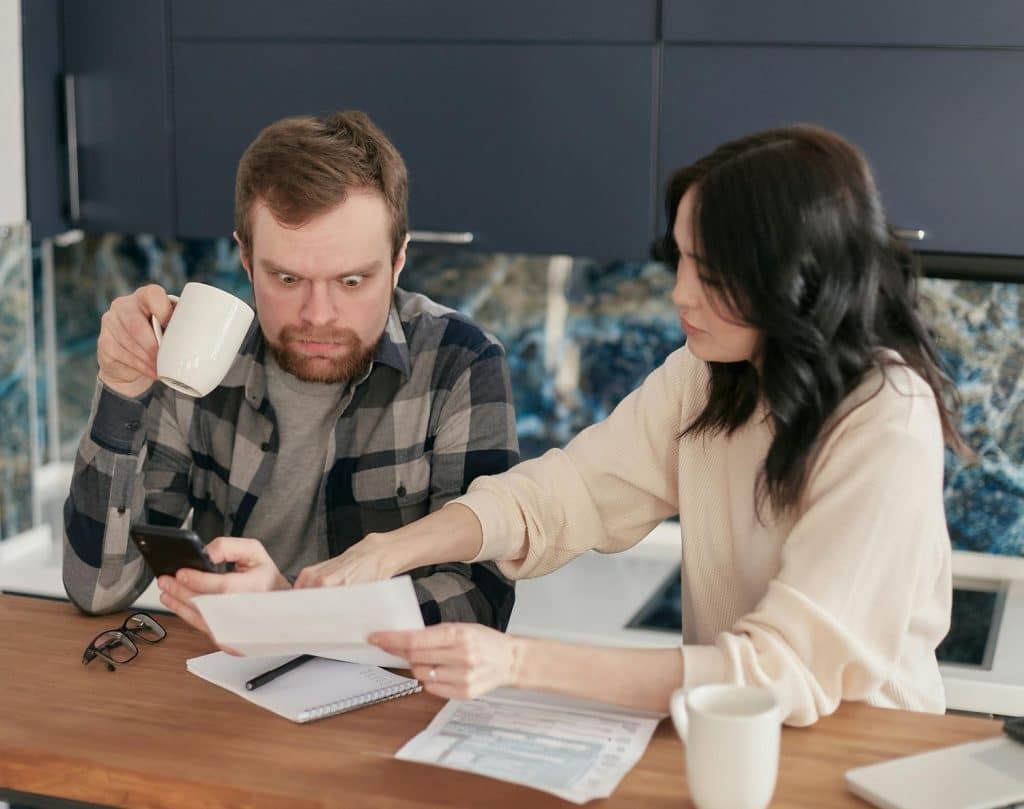 A couple reviewing household bills and rent statements at the kitchen table, looking concerned while verifying if utilities are included in rent.