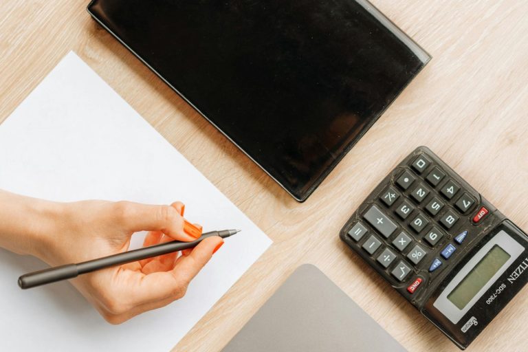 Person calculating pro rata pay using a calculator and taking notes on a desk with a tablet and paper.