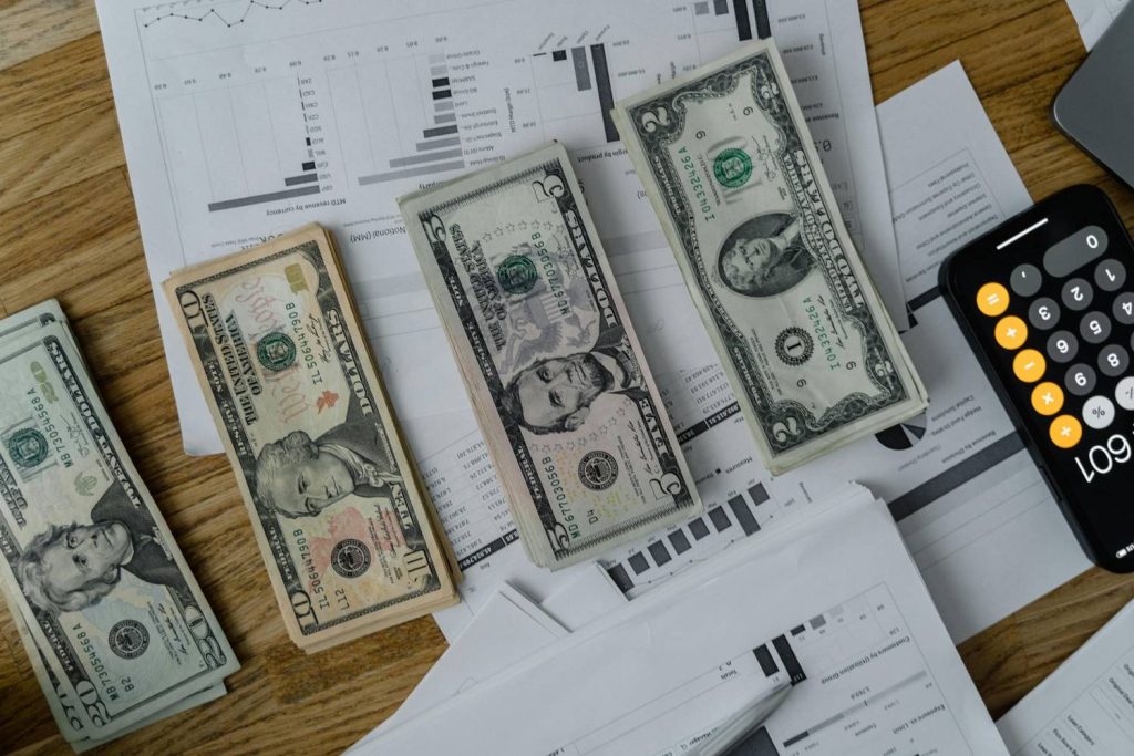 Stacks of U.S. dollar bills, financial documents, and a calculator on a desk showing savings planning for a rainy day fund.