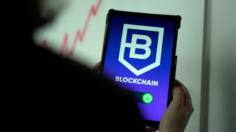 Person holding a tablet displaying a blockchain logo and app interface with rising market graph in the background.