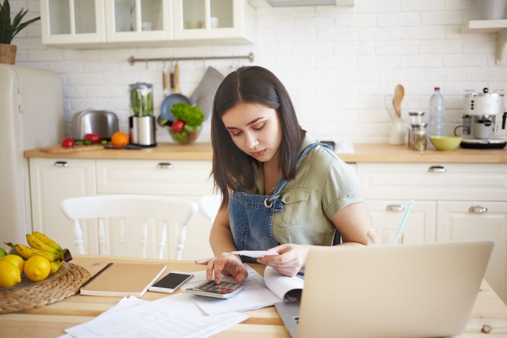 A woman at her kitchen table calculating monthly payments based on a specific APR.