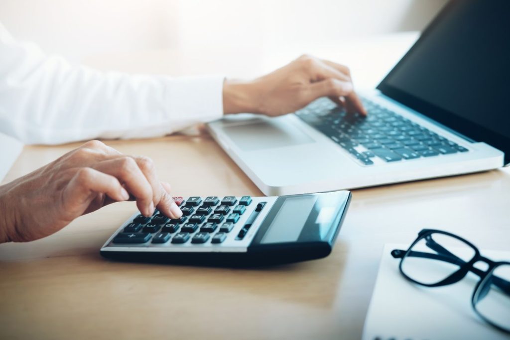 An accountant using a calculator and laptop to determine a client's annual interest rate.