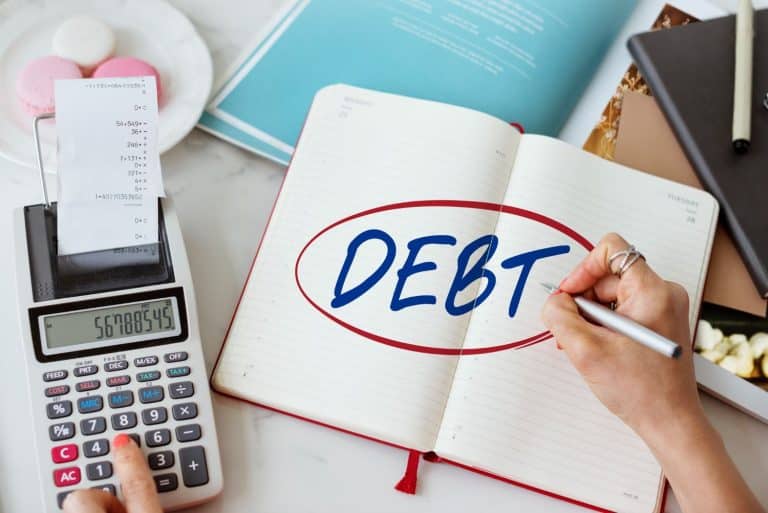 Person using a calculator and notebook to total balances when applying for personal loans for debt consolidation.