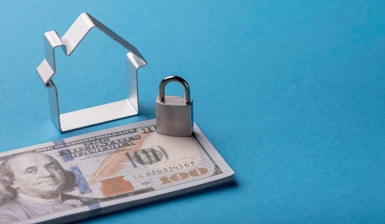 A model house placed on a stack of banknotes, representing property used as collateral for a secured loan.