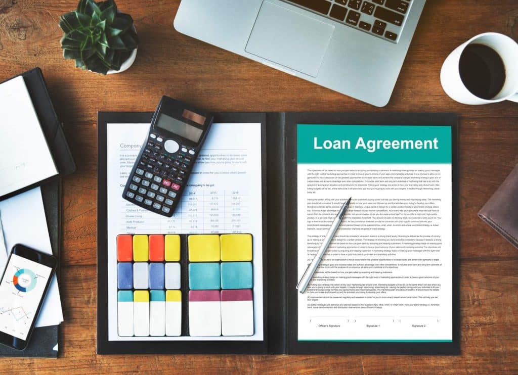 Hands holding a house model and cash over a contract, symbolizing the assets in a secured loan.