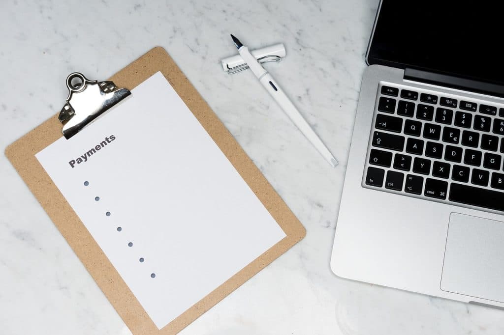 A blank payments checklist on a clipboard next to a laptop, representing organized financial planning.