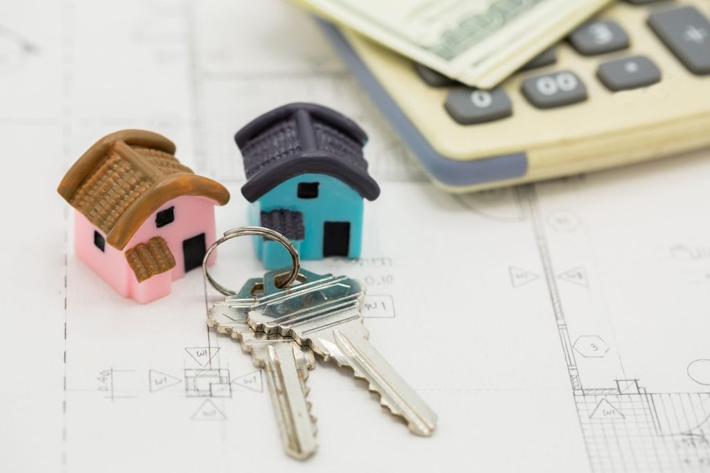 A real estate purchase contract on a desk with $100 bills and house keys to define what is a mortgage cost.