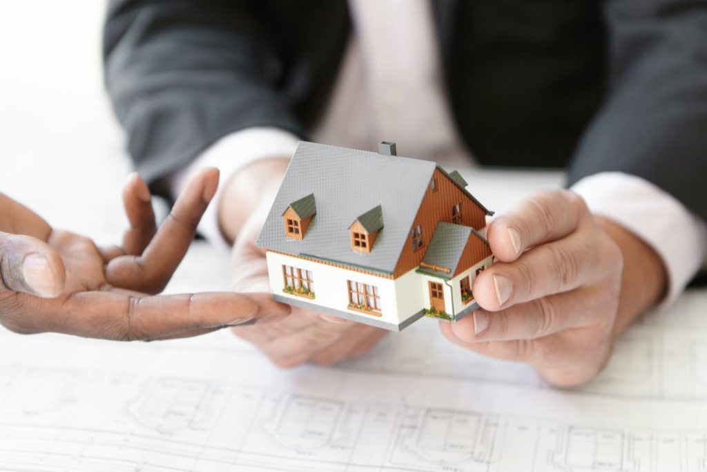 Two people holding a small house model over architectural plans, illustrating what is a mortgage for a home.