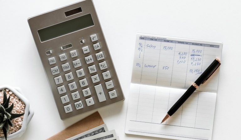 Top view of calculator beside paper and pen with money under for debt-to-income ratio calculation.