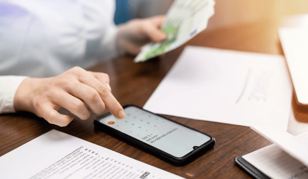 A woman uses a smartphone calculator and holds cash to calculate an origination fee for her finances.