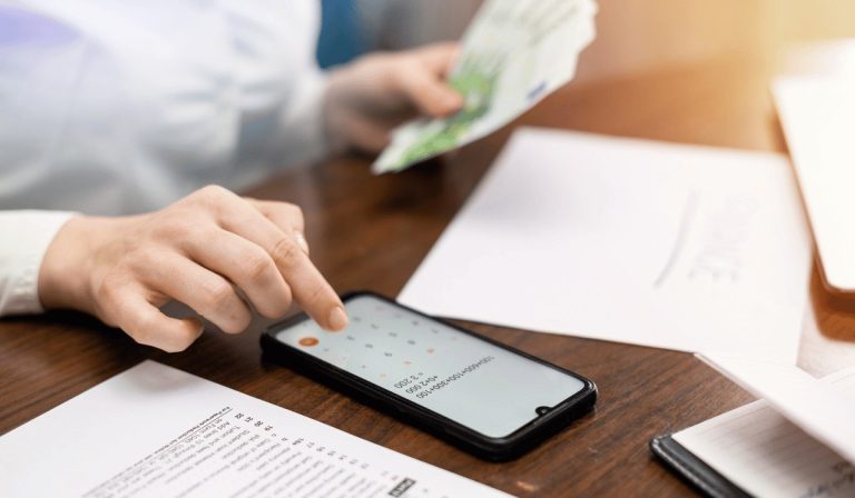 A woman uses a smartphone calculator and holds cash to calculate an origination fee for her finances.
