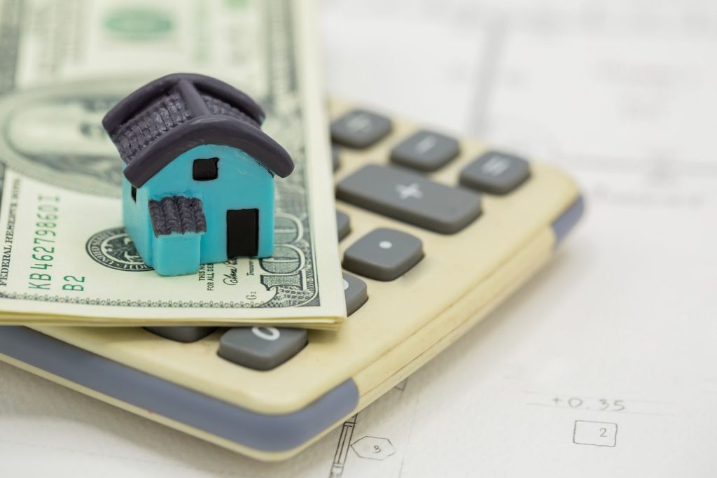 A small blue model house on a calculator and cash used to estimate monthly FHA mortgage payments.