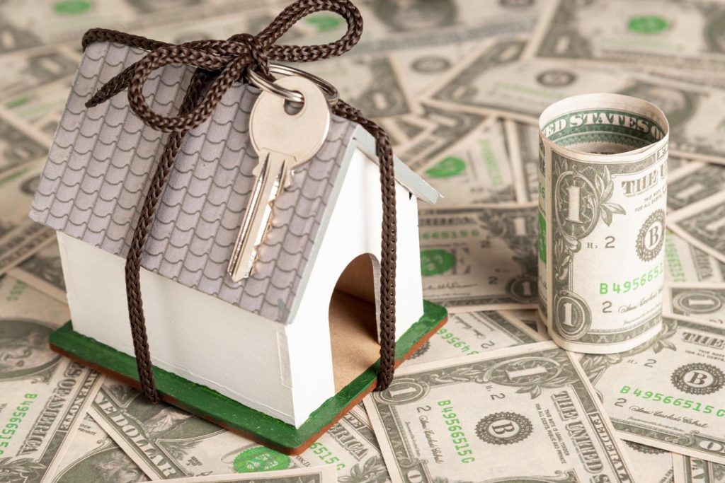 A model house wrapped in cord with keys on a bed of cash, illustrating the results of a cash-out refinance.